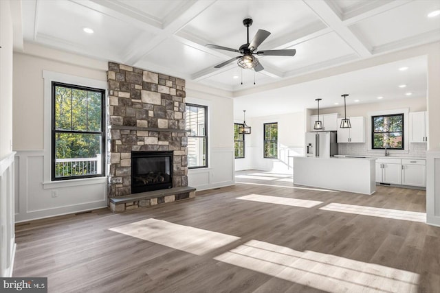 unfurnished living room with a stone fireplace, coffered ceiling, a sink, and light wood-style floors