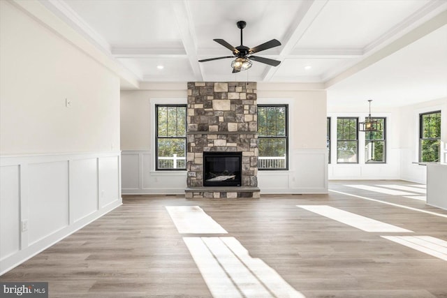 unfurnished living room featuring light wood-type flooring, plenty of natural light, beamed ceiling, and a stone fireplace