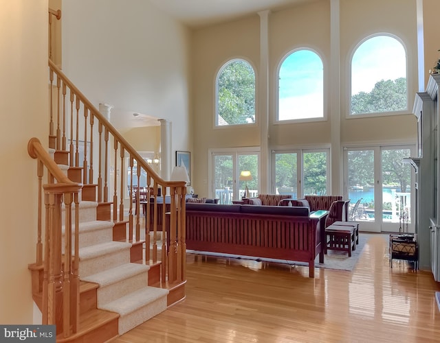 living room featuring a towering ceiling, a healthy amount of sunlight, wood finished floors, and stairs