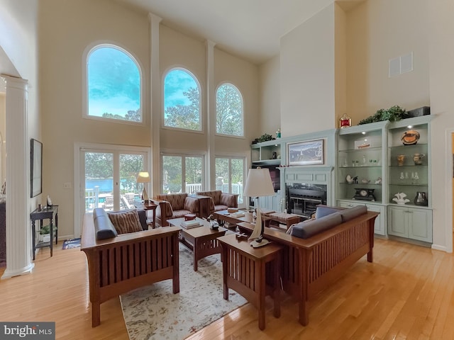 living room with ornate columns, a glass covered fireplace, visible vents, and light wood finished floors