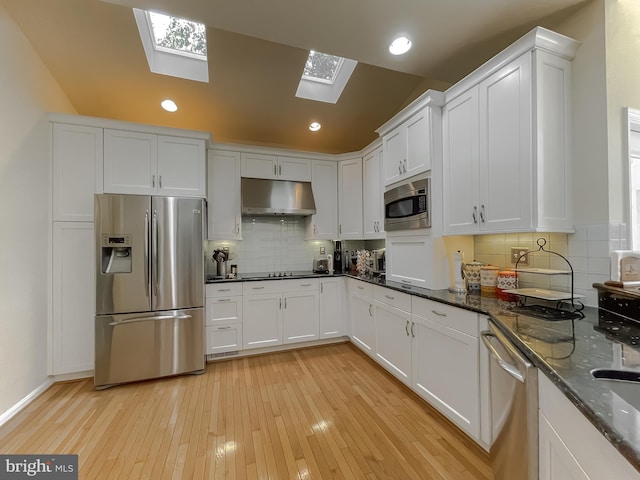 kitchen featuring light wood finished floors, backsplash, under cabinet range hood, white cabinets, and stainless steel appliances