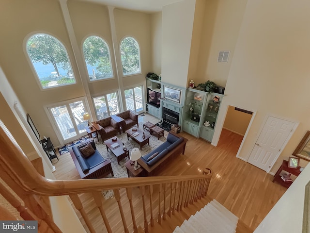 living area featuring visible vents, wood finished floors, a high ceiling, and a glass covered fireplace