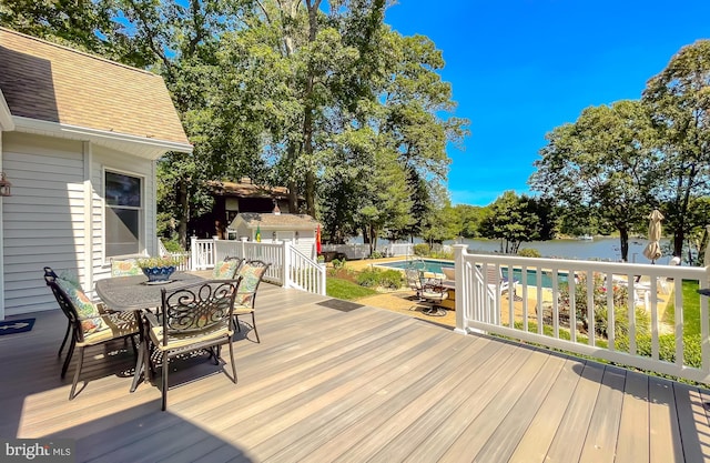 wooden terrace featuring outdoor dining space, an outdoor structure, a fenced in pool, and a water view