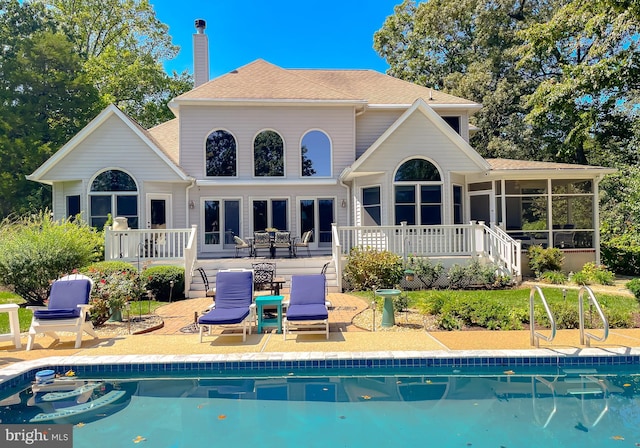 rear view of house with a patio, a sunroom, a shingled roof, an outdoor pool, and a chimney