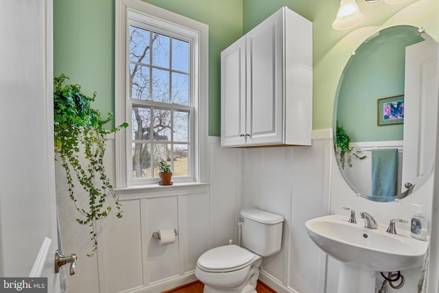 bathroom featuring plenty of natural light, wainscoting, toilet, and a sink