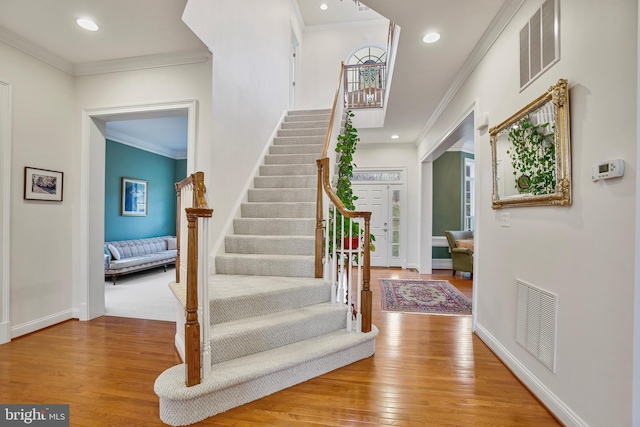 foyer entrance with hardwood / wood-style floors, crown molding, baseboards, and visible vents