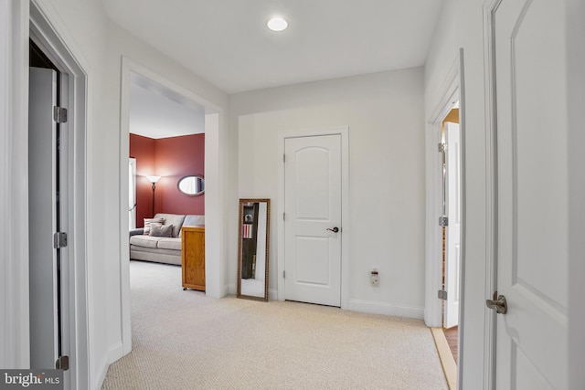 hallway featuring light colored carpet and baseboards