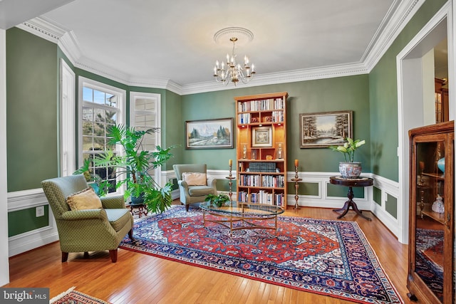 living area featuring crown molding, wainscoting, wood-type flooring, and a chandelier