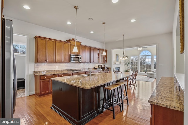 kitchen with light wood-style flooring, light stone counters, stainless steel appliances, brown cabinetry, and decorative backsplash