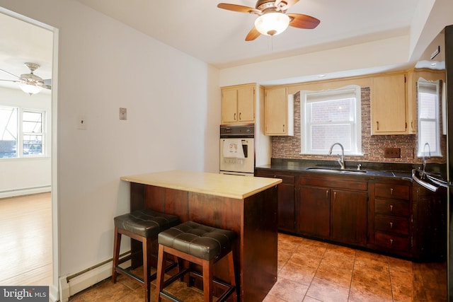 kitchen featuring a kitchen bar, a sink, a baseboard heating unit, backsplash, and white oven