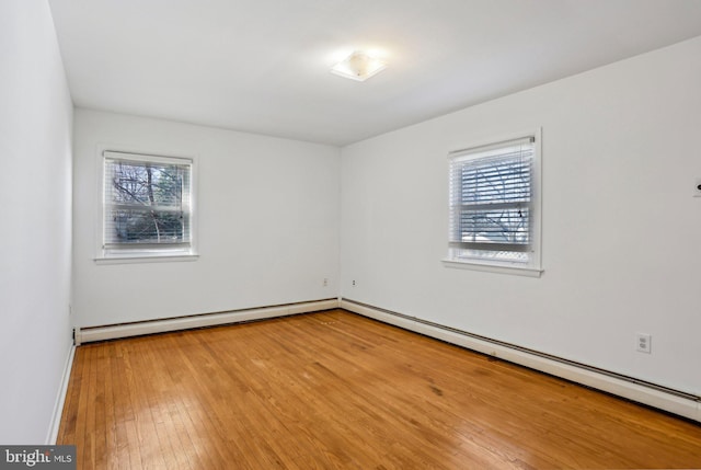 spare room with a baseboard heating unit, baseboard heating, a healthy amount of sunlight, and hardwood / wood-style flooring