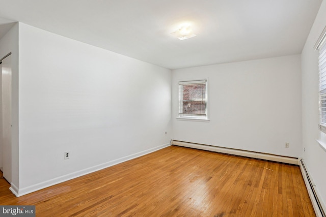 unfurnished room featuring wood finished floors, baseboards, and a baseboard radiator