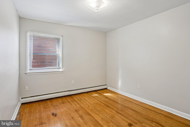 spare room featuring a baseboard heating unit, baseboards, and wood finished floors