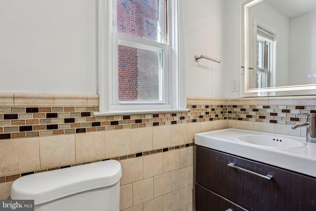 half bath featuring tile walls, wainscoting, toilet, and vanity