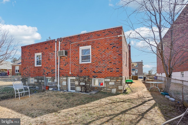 rear view of house featuring a wall mounted air conditioner, a yard, brick siding, and a fenced backyard