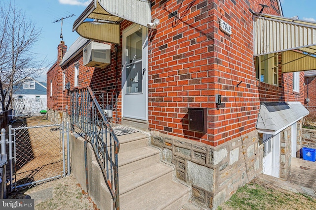 doorway to property with a gate, brick siding, a wall mounted air conditioner, and fence