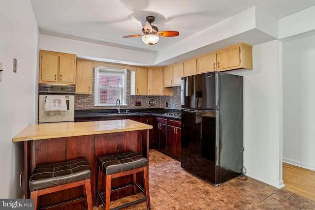 kitchen featuring a kitchen bar, decorative backsplash, freestanding refrigerator, white oven, and a sink