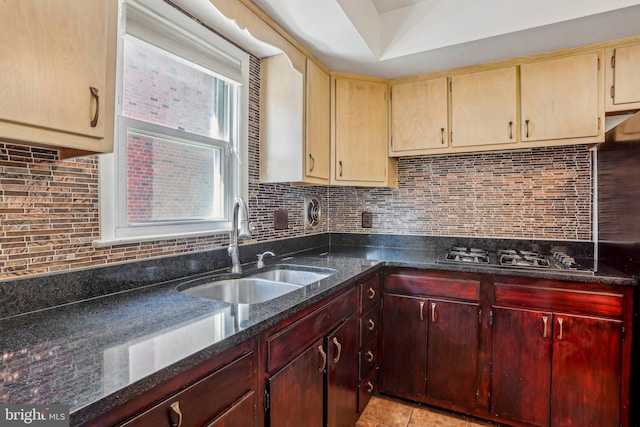 kitchen featuring tasteful backsplash, dark stone counters, gas cooktop, and a sink