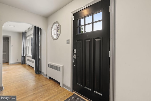 entryway featuring radiator heating unit, arched walkways, light wood-type flooring, and baseboards