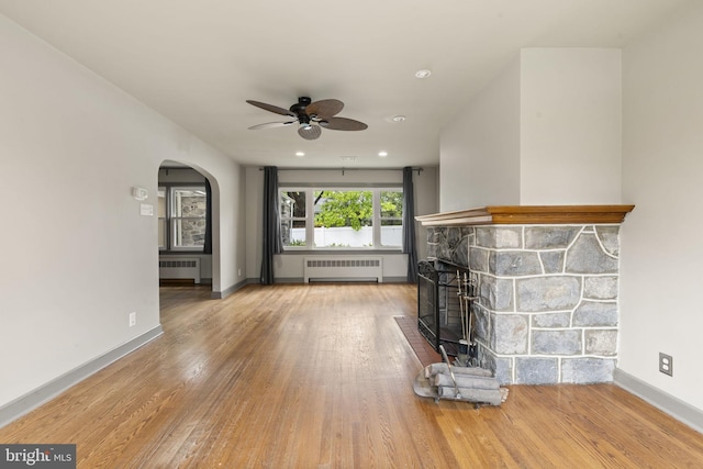 unfurnished living room featuring radiator, ceiling fan, wood finished floors, arched walkways, and recessed lighting