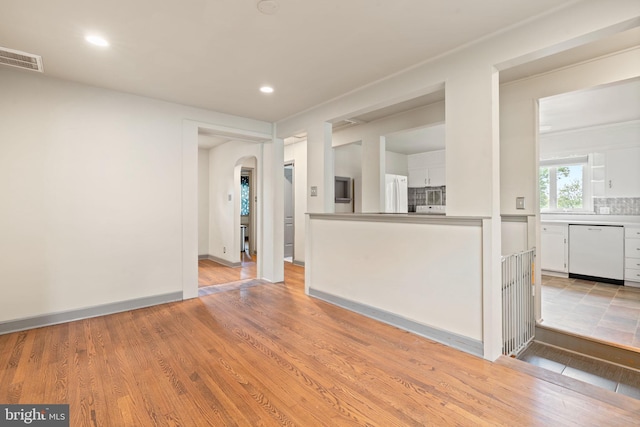 unfurnished living room featuring arched walkways, recessed lighting, light wood finished floors, and baseboards