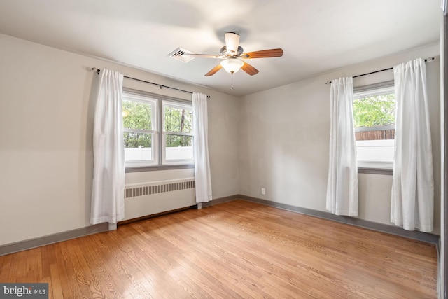 unfurnished room with radiator, plenty of natural light, ceiling fan, and light wood-style floors