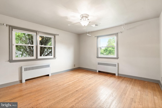 empty room with radiator, a ceiling fan, wood finished floors, and baseboards