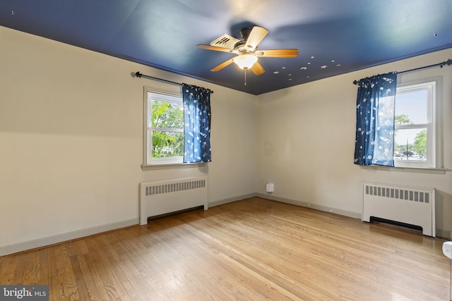 empty room with radiator heating unit, a ceiling fan, wood finished floors, and baseboards