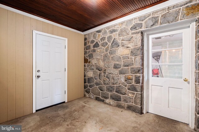 entryway with crown molding, wooden walls, and unfinished concrete flooring