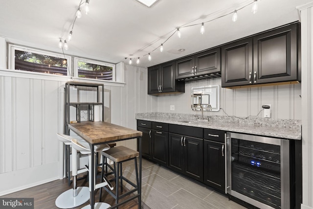 kitchen featuring wine cooler, a sink, dark cabinets, light stone counters, and track lighting