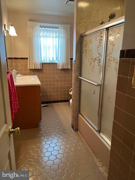 full bath featuring tile patterned floors, shower / bath combination with glass door, tile walls, and vanity