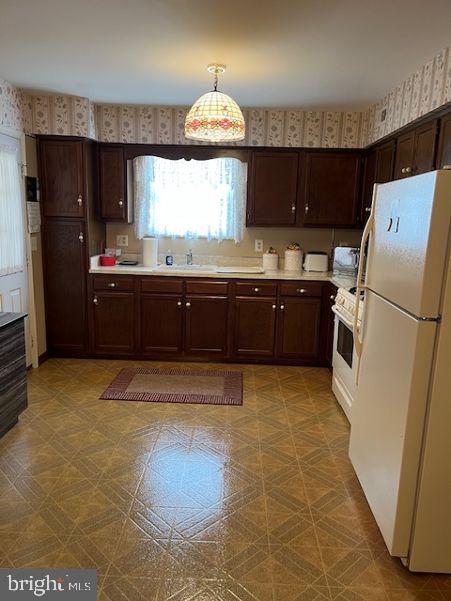 kitchen featuring dark brown cabinets, white appliances, wallpapered walls, and light countertops