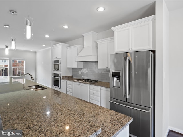 kitchen featuring white cabinets, a sink, stainless steel appliances, premium range hood, and backsplash