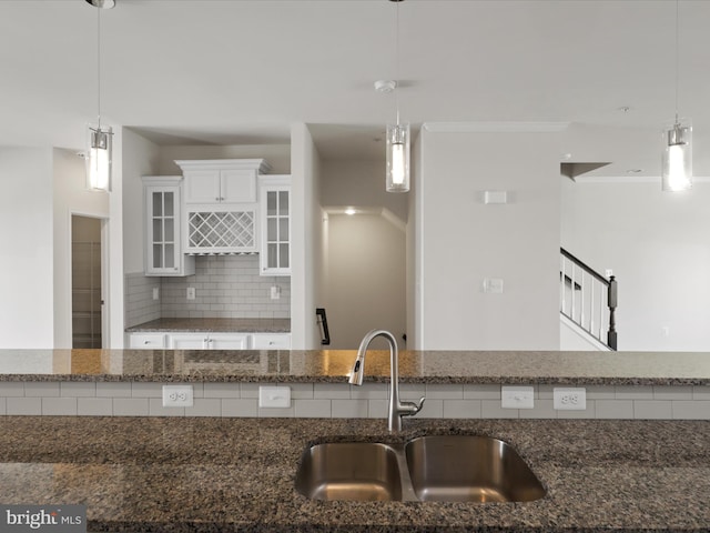 kitchen featuring a sink, white cabinets, decorative backsplash, dark stone countertops, and crown molding