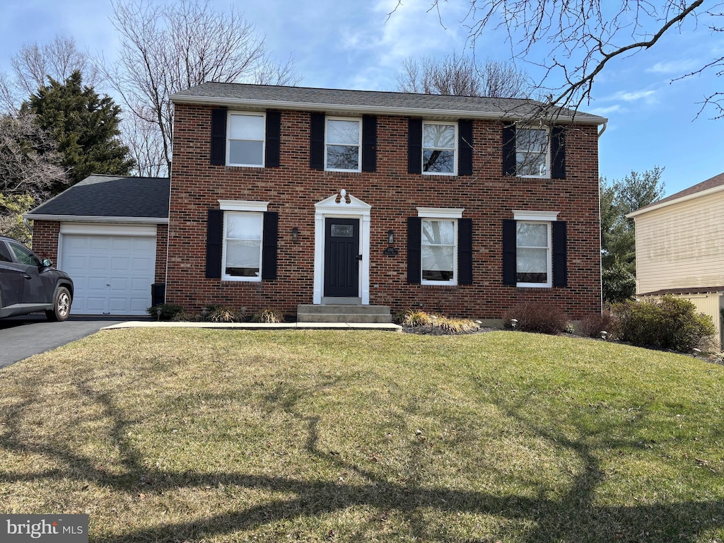 colonial home featuring a garage, brick siding, a front lawn, and aphalt driveway