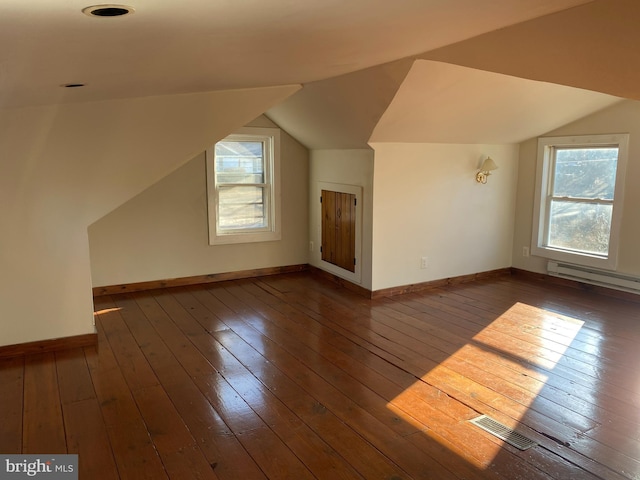 additional living space featuring a baseboard heating unit, vaulted ceiling, visible vents, and dark wood finished floors