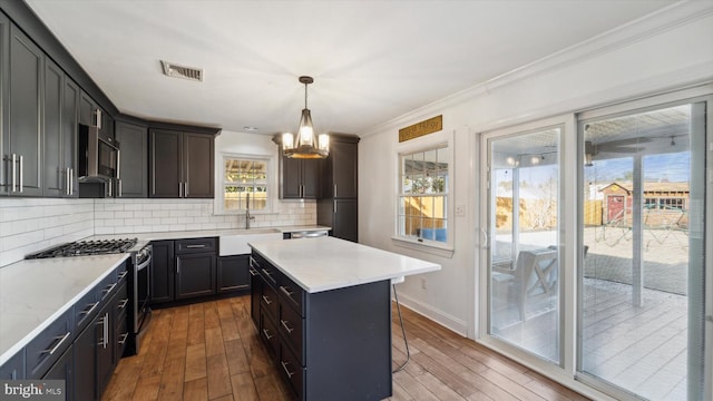 kitchen with stainless steel appliances, a sink, visible vents, backsplash, and wood-type flooring