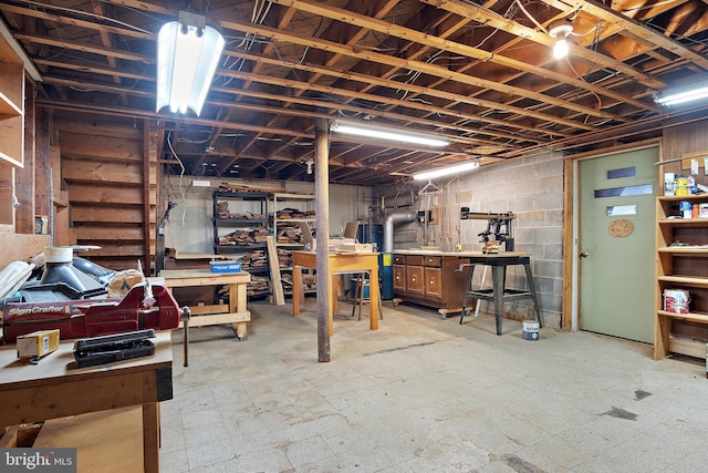 unfinished basement featuring tile patterned floors, water heater, concrete block wall, and a workshop area