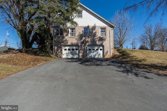 view of property exterior featuring driveway, an attached garage, and brick siding