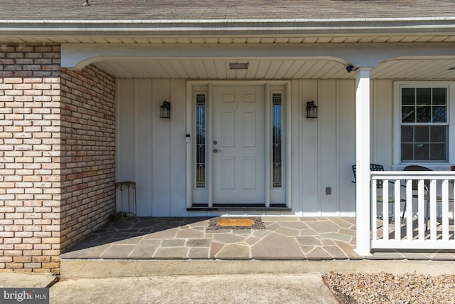 property entrance featuring a porch, roof with shingles, and brick siding