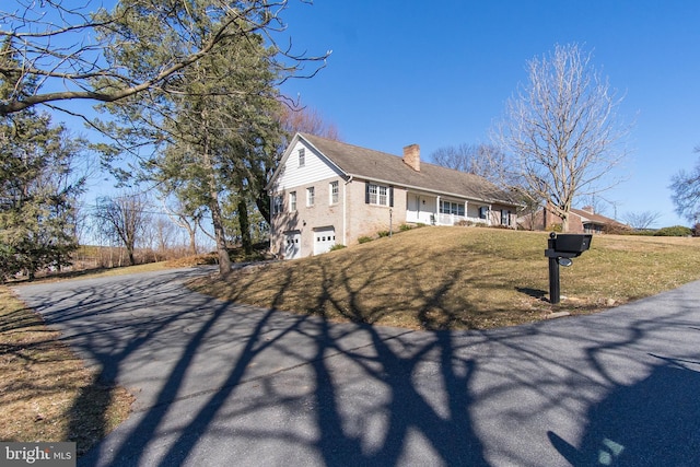 view of front of home featuring driveway, a chimney, a front lawn, and brick siding