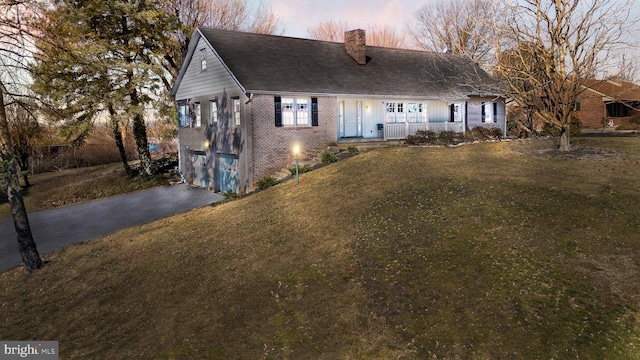 view of front facade with brick siding, a yard, a chimney, an attached garage, and driveway