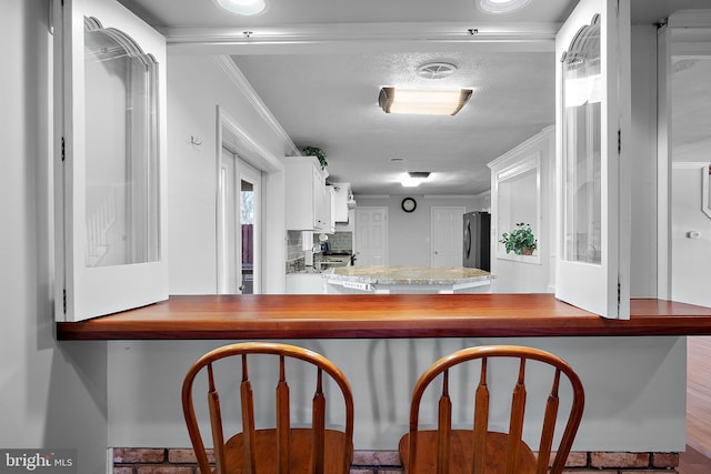 kitchen featuring crown molding, decorative backsplash, freestanding refrigerator, white cabinetry, and a peninsula