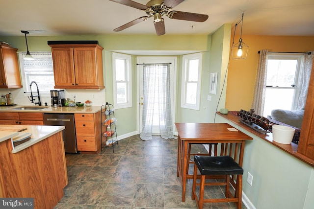 kitchen with light countertops, hanging light fixtures, a sink, dishwasher, and baseboards