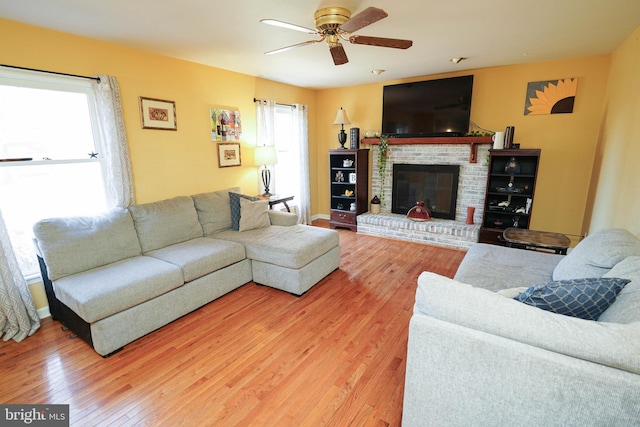 living room with a brick fireplace, ceiling fan, and wood finished floors