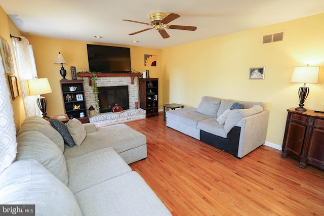 living area with light wood finished floors, baseboards, visible vents, a ceiling fan, and a fireplace