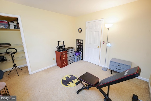 workout area with baseboards and light colored carpet