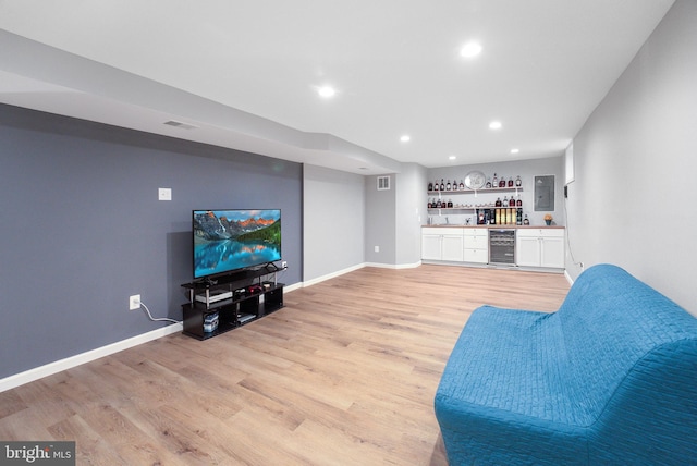 living room with visible vents, light wood-style flooring, beverage cooler, wet bar, and baseboards