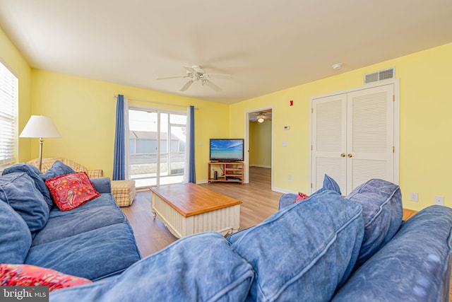 living room featuring ceiling fan, visible vents, baseboards, and wood finished floors