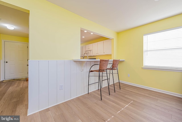 kitchen featuring white microwave, a kitchen bar, a peninsula, light wood-style floors, and white cabinetry